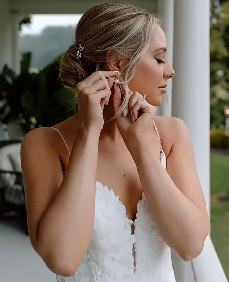 Bride in a lace gown fastening her earring on a porch, soft glam makeup