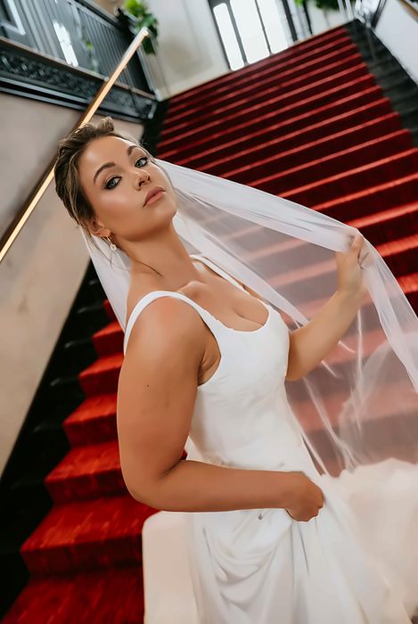 Bride with a veil on a red carpeted staircase, polished bridal makeup
